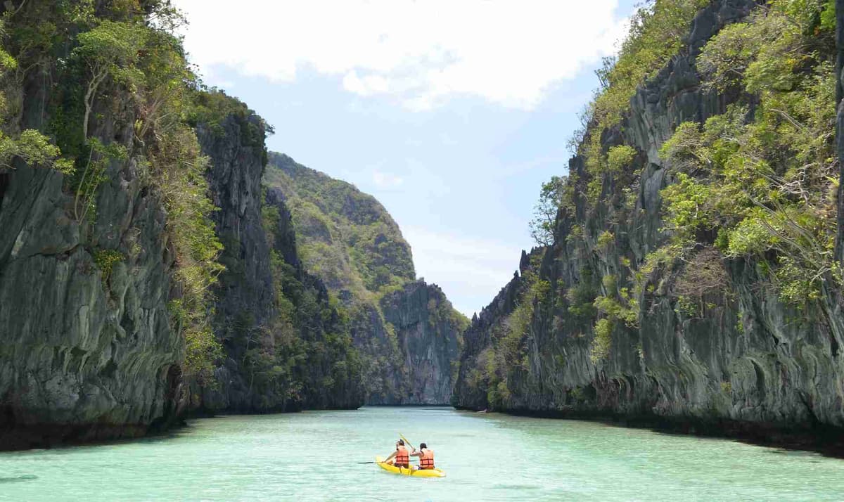Kayakers on turquoise water with towering cliffs.