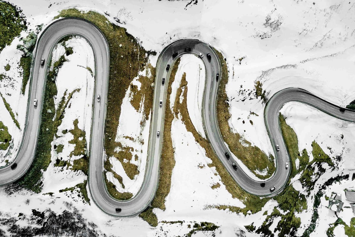 Aerial shot of a serpentine road with cars amidst snowy patches.