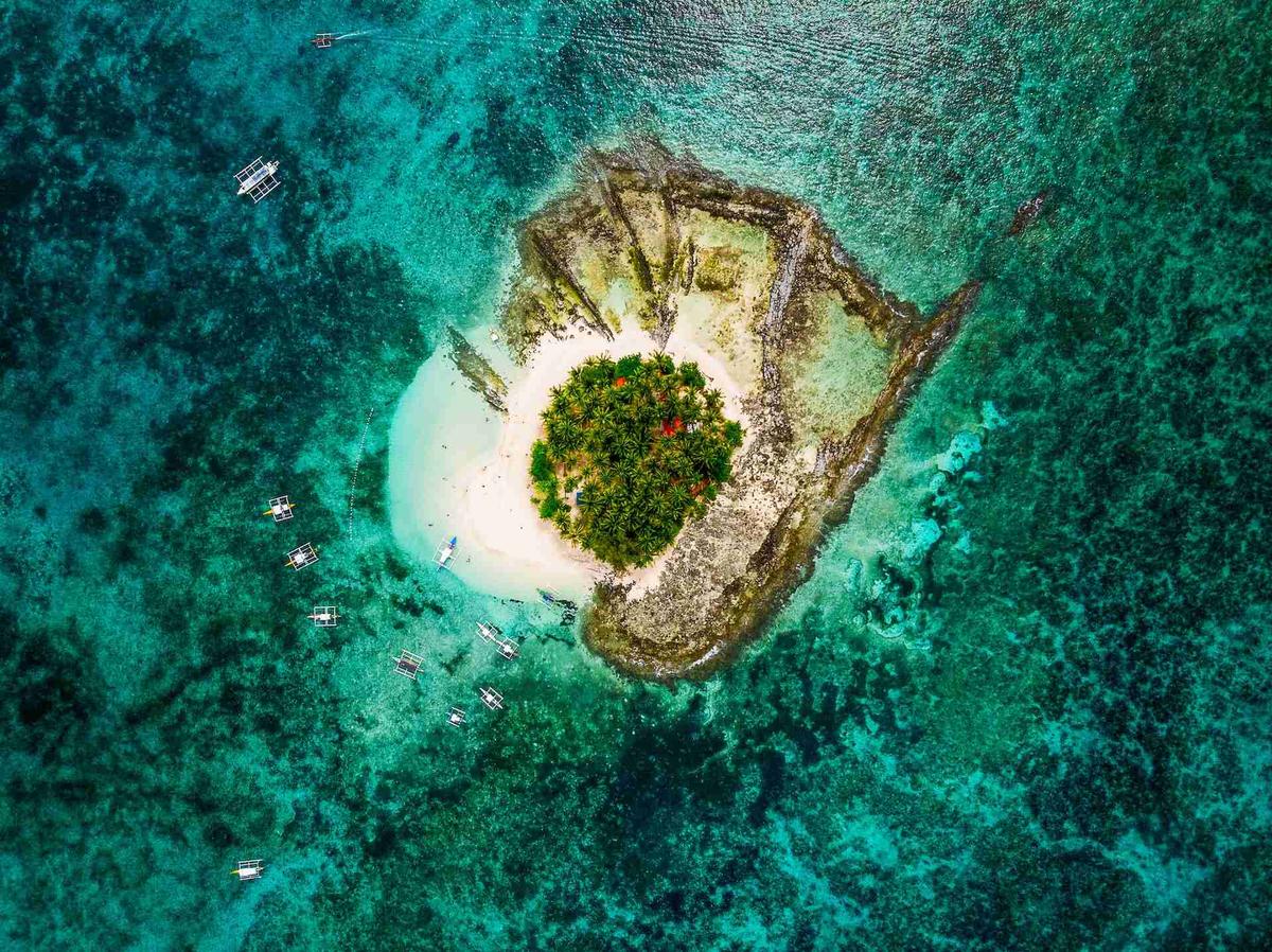 Aerial view of a small, palm-fringed island surrounded by coral reefs.