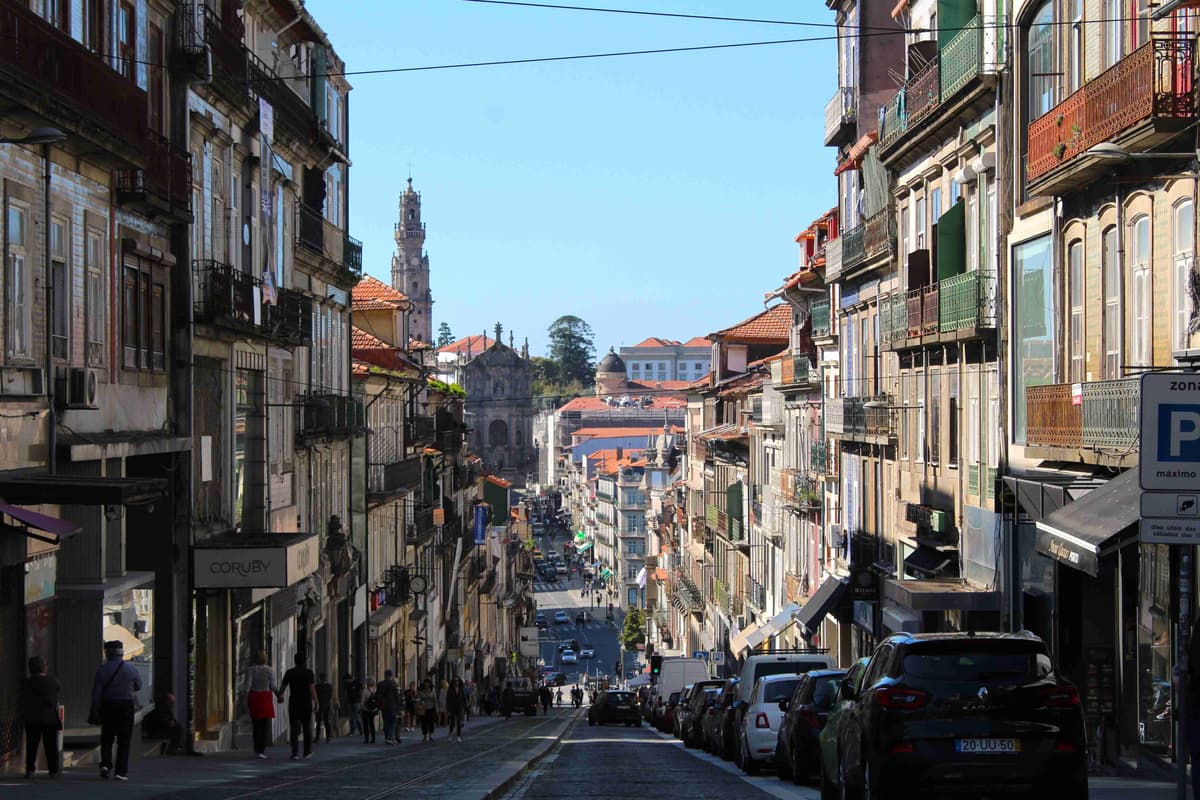 View of Rua dos Clérigos ,with pedestrians and parked cars, Clérigos Tower under a clear blue sky.