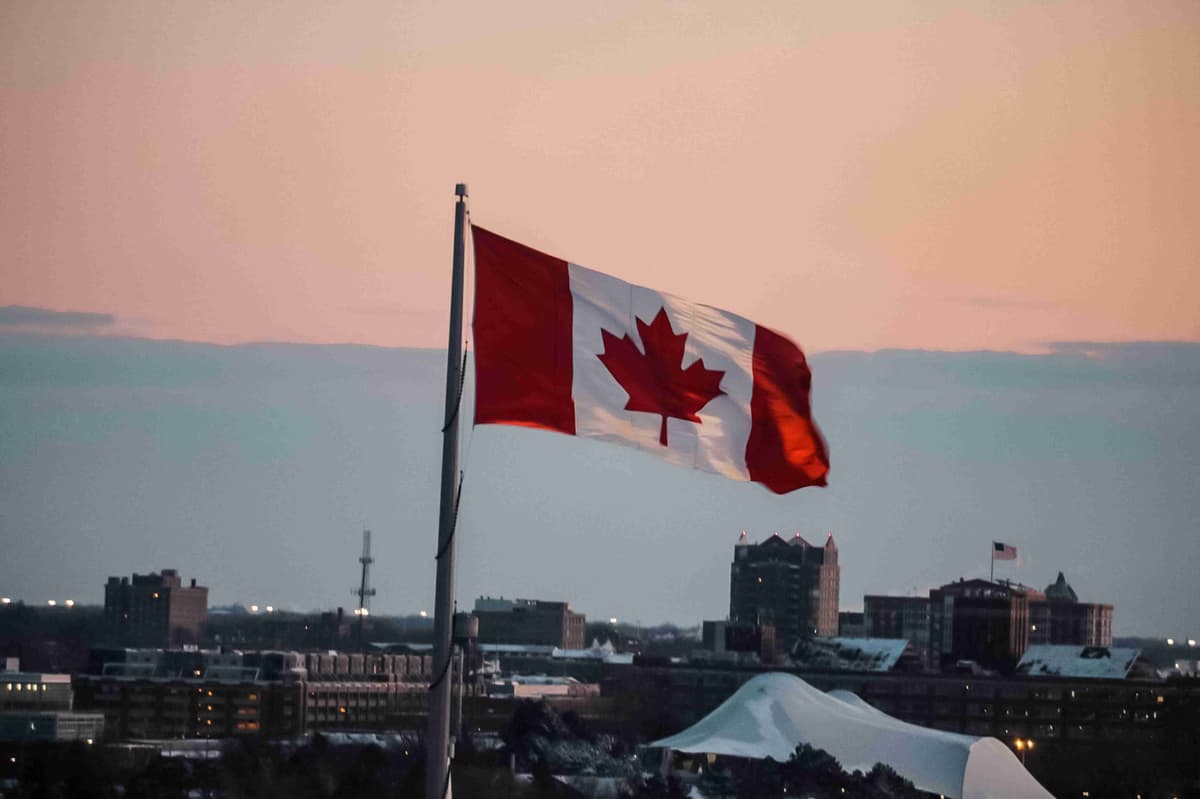 Canadian flag waving at sunset with city skyline in the background.
