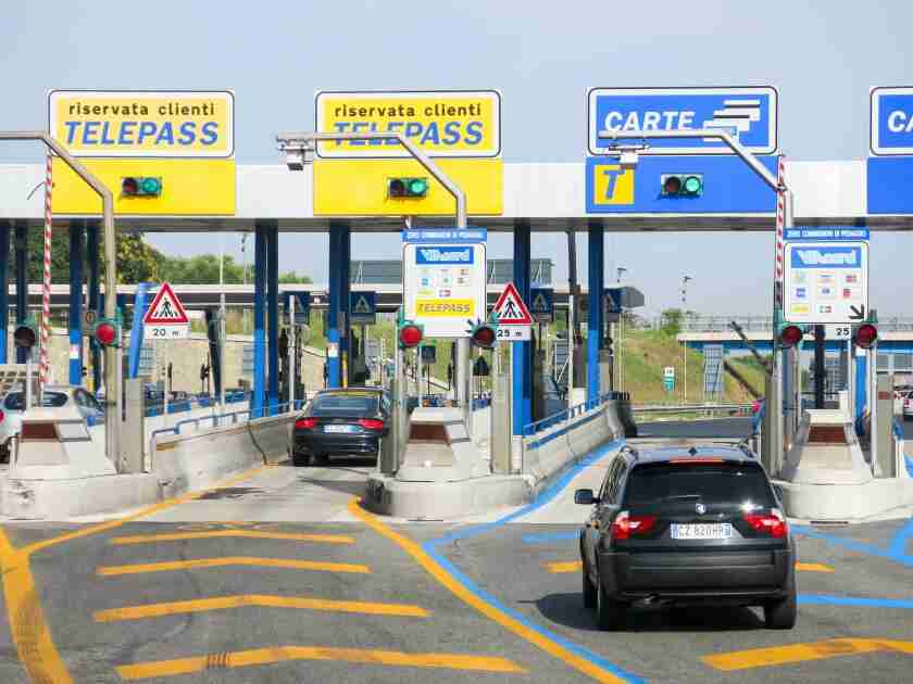 Cars at Telepass toll lanes in Italy, signs indicating pass access.
