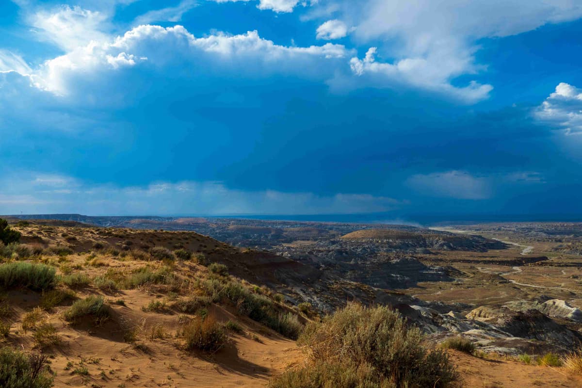 Vista ampla do deserto com céu dramático e chuva à distância