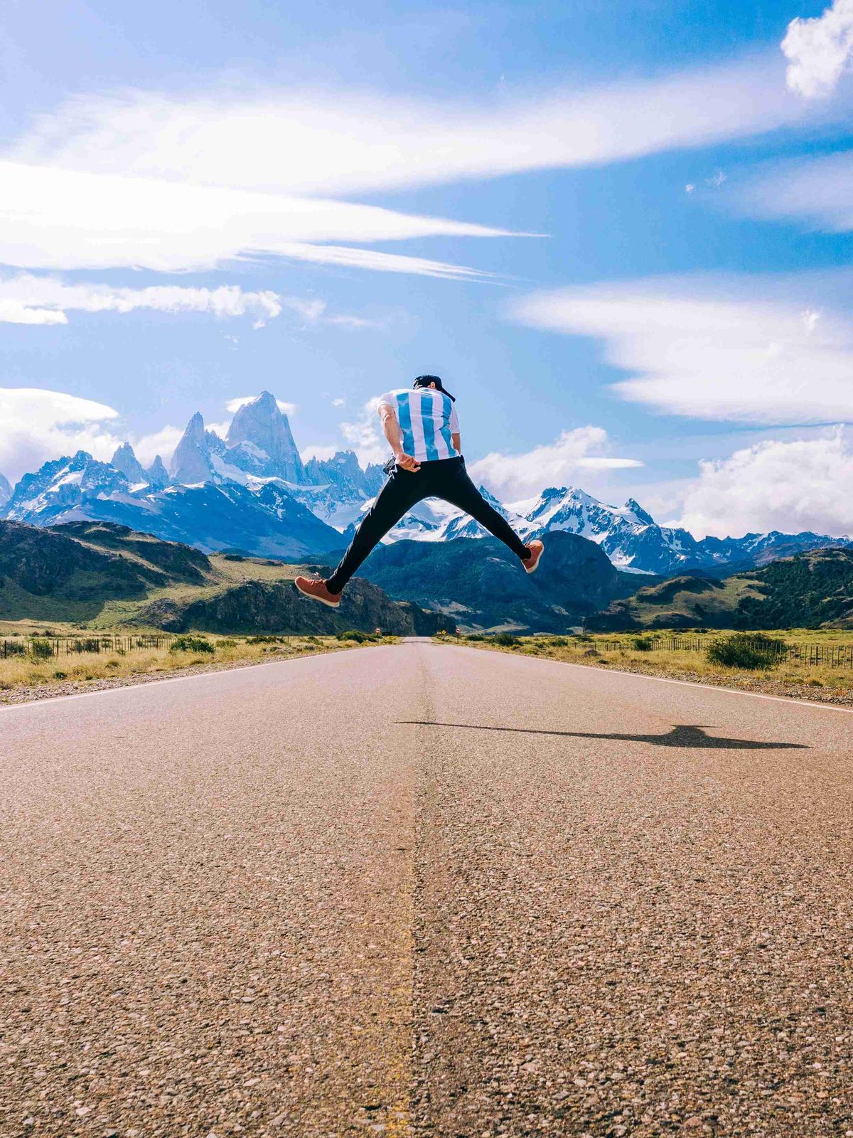 Exuberant Jump on Mountain Road with Snowy Peaks in Background