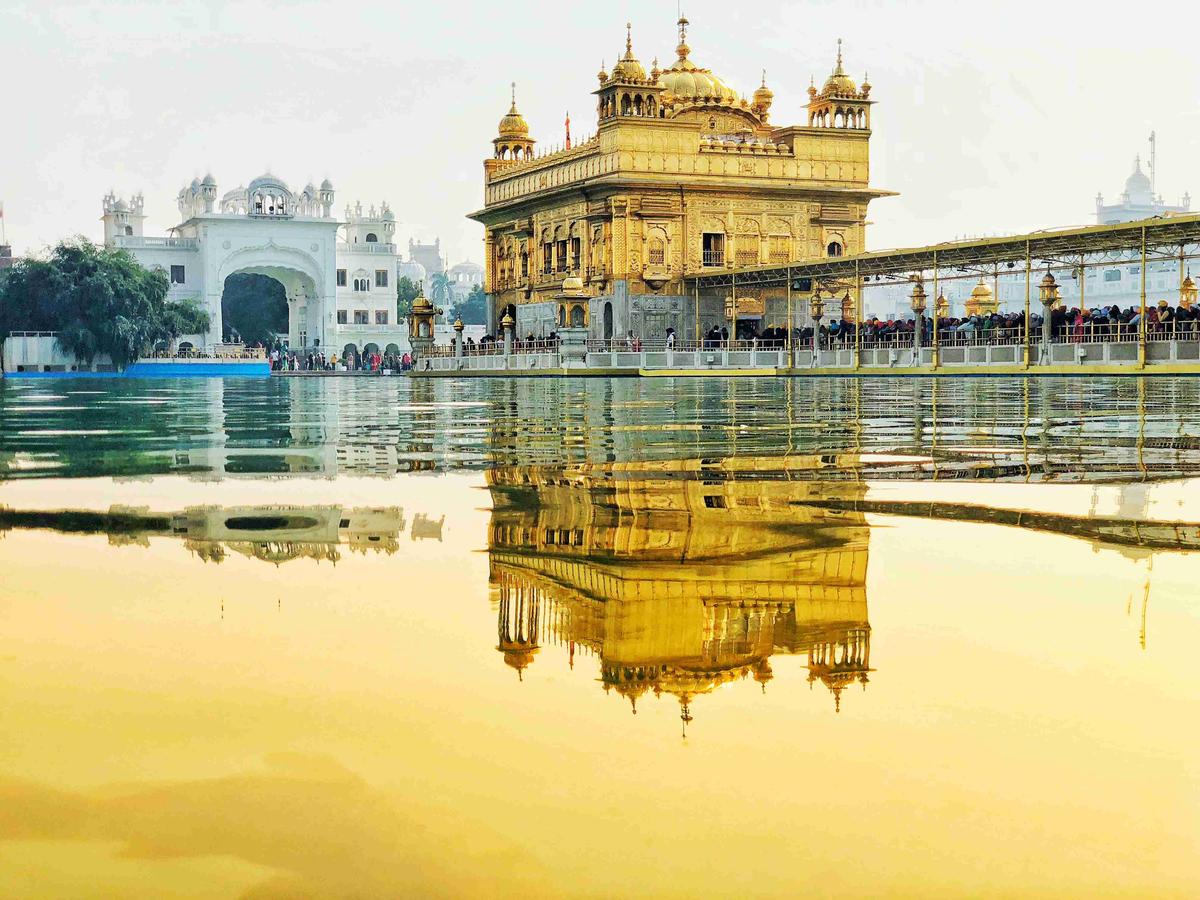 The golden temple in amritsar is reflected in water.