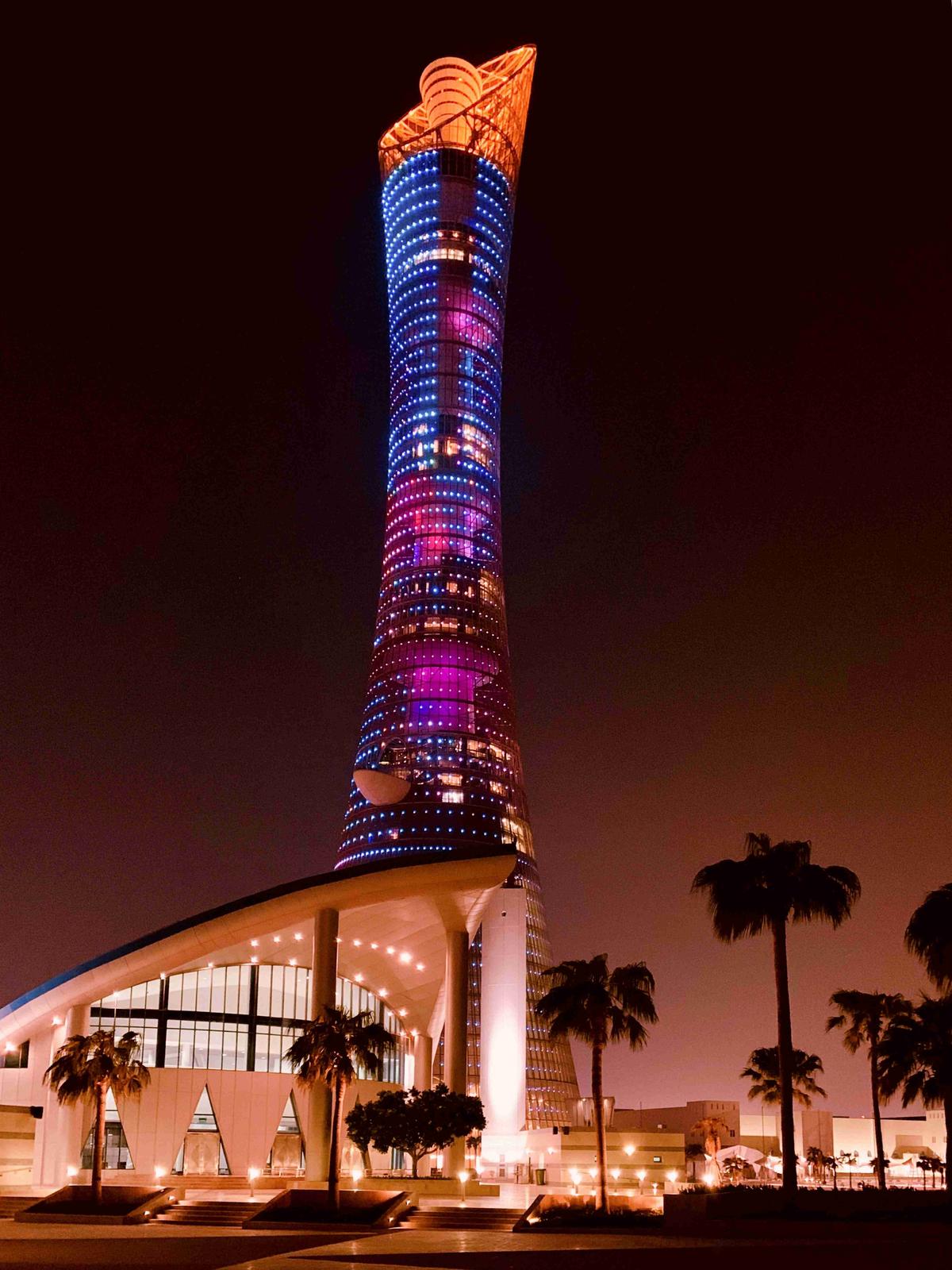 Illuminated Twisting Tower at Night with Palm Trees