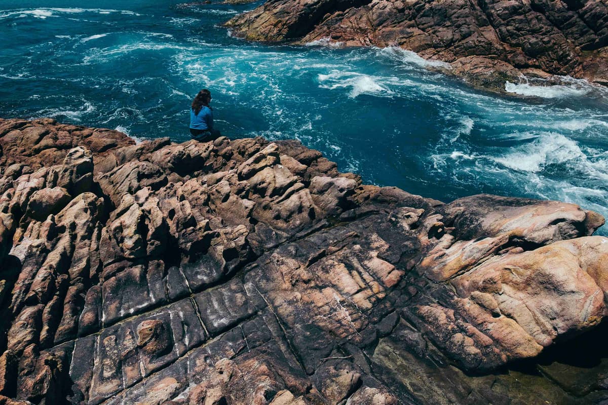 A person standing on a rocky cliff overlooking the body of water.