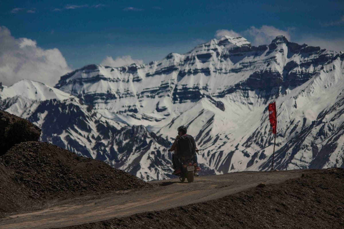 Motorcyclist Riding Towards Snowy Mountain Peaks