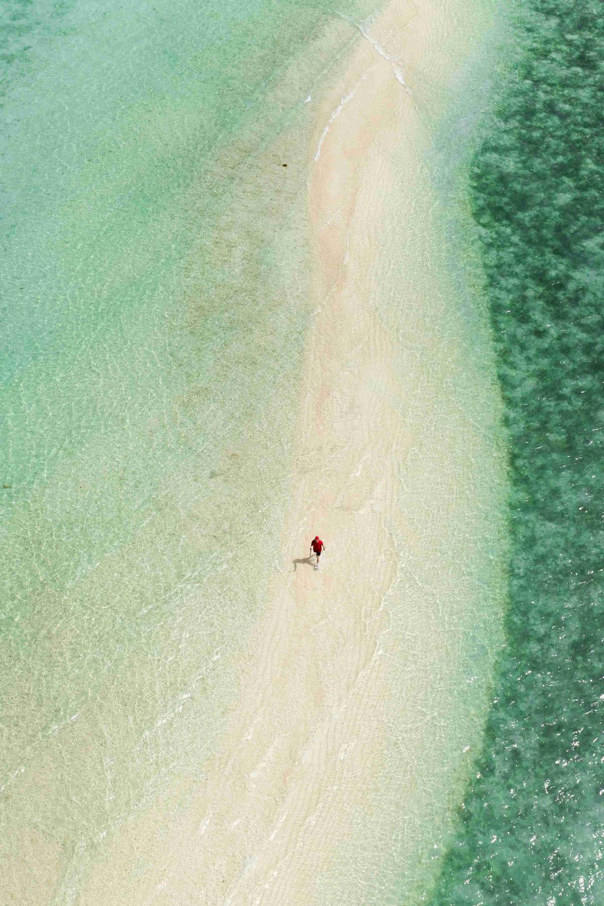 Person Walking on Sandbar Between Turquoise Waters