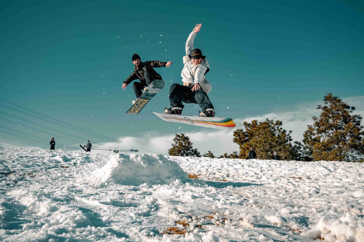 Snowboarders Jumping Together on Snowy Hill