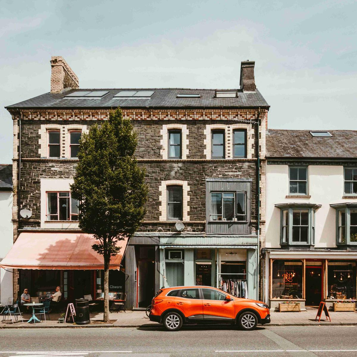 Vista de la calle con edificios de piedra y coche naranja.