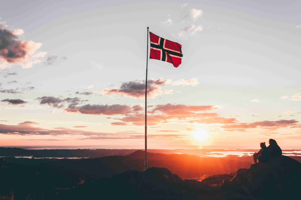Vista do pôr do sol com bandeira norueguesa e figuras em silhueta