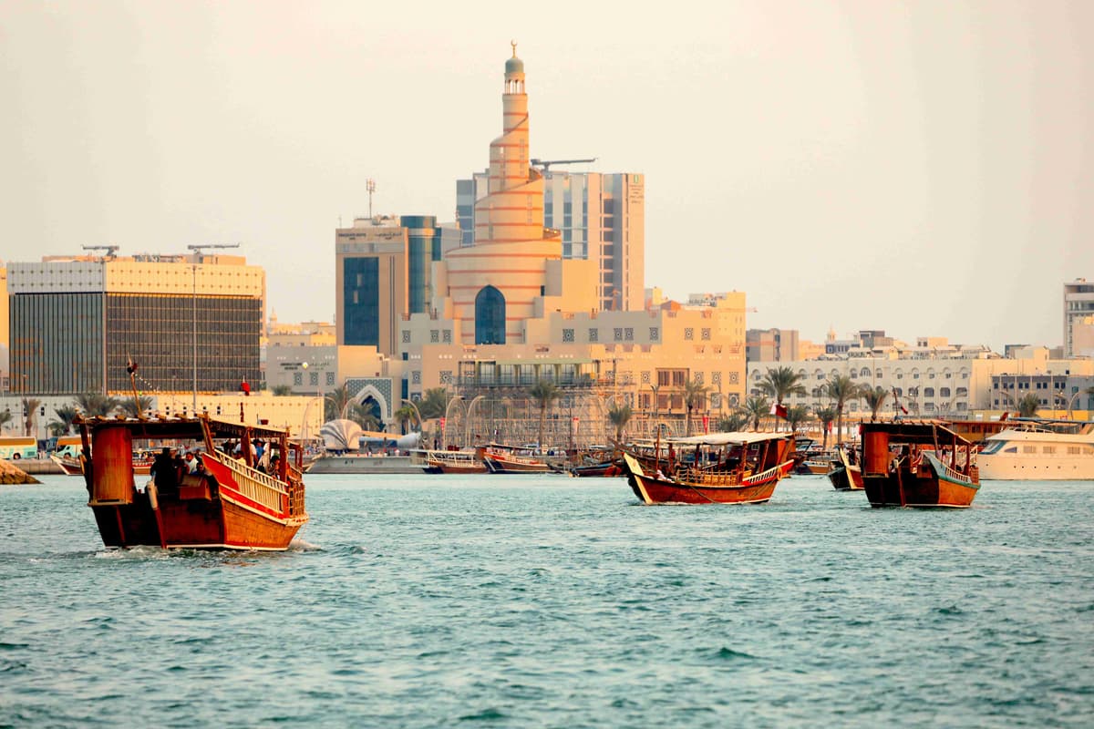 Perahu Tradisional di Tepi Laut dengan Latar Belakang Kota Modern saat Matahari Terbenam