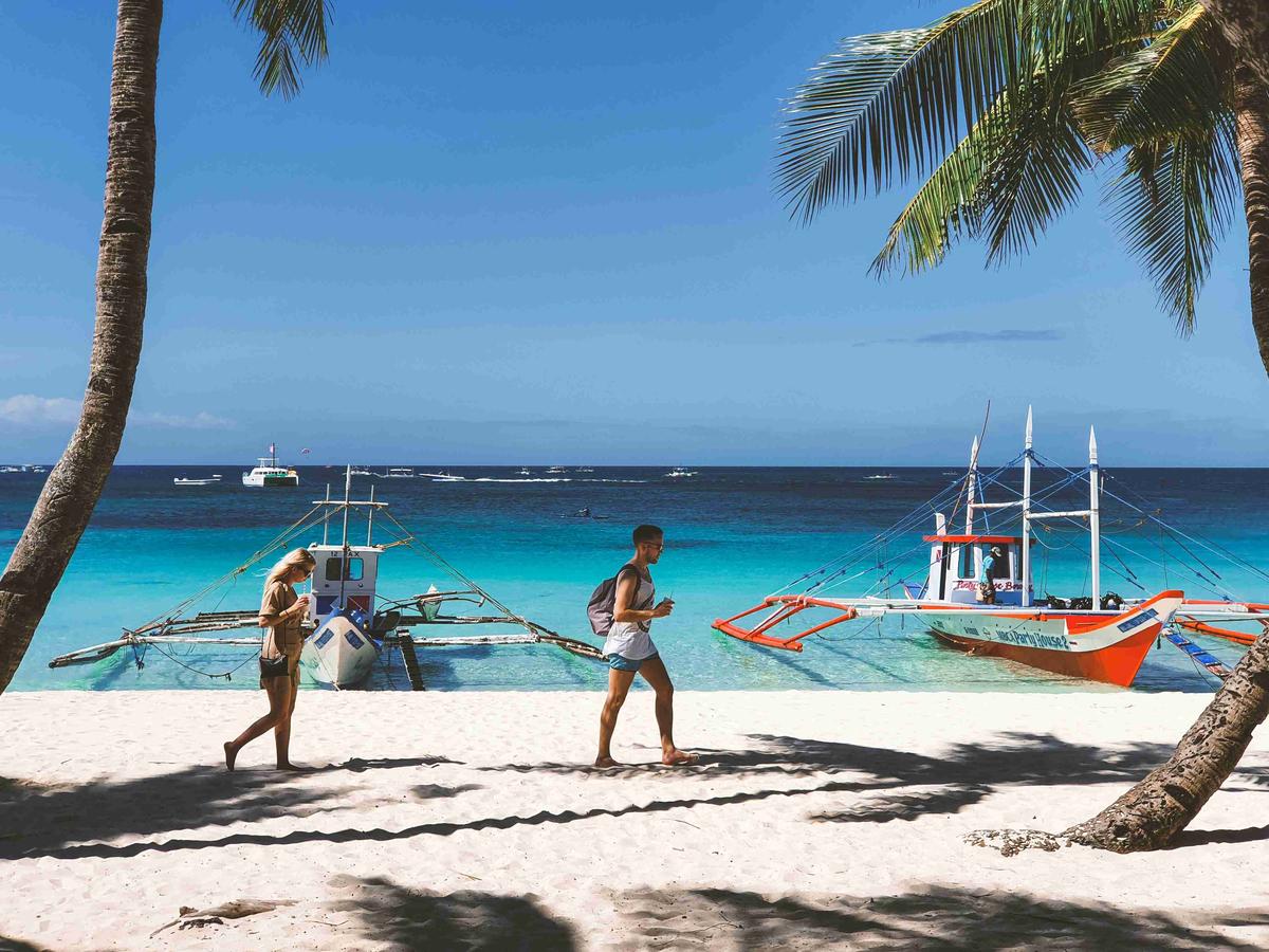 Plaja tropicală cu turiști și bărci tradiționale filipineze