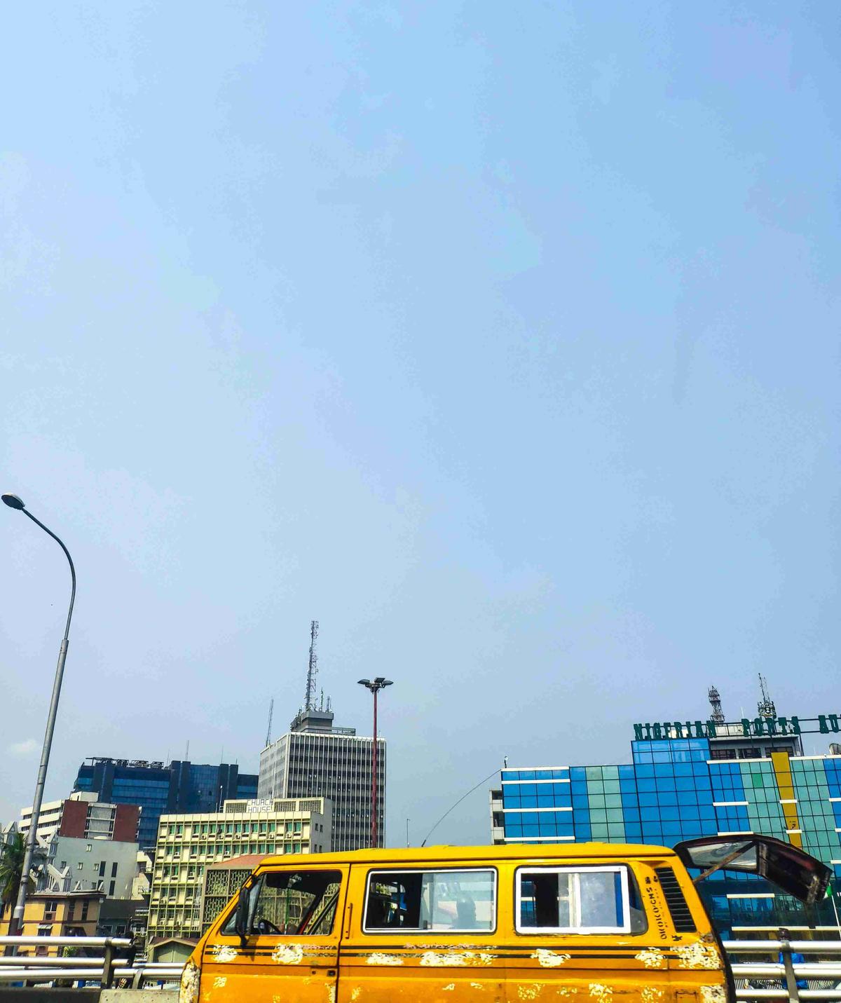 Dzeltens autobuss pilsētas ainavā ar modernām ēkām pret skaidrām debesīm