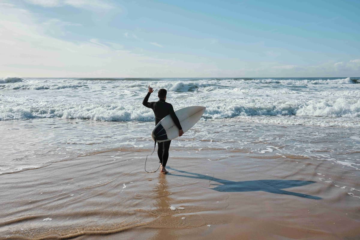 en-mand-holder-et-surfbræt-på-toppen-af-en-sandstrand