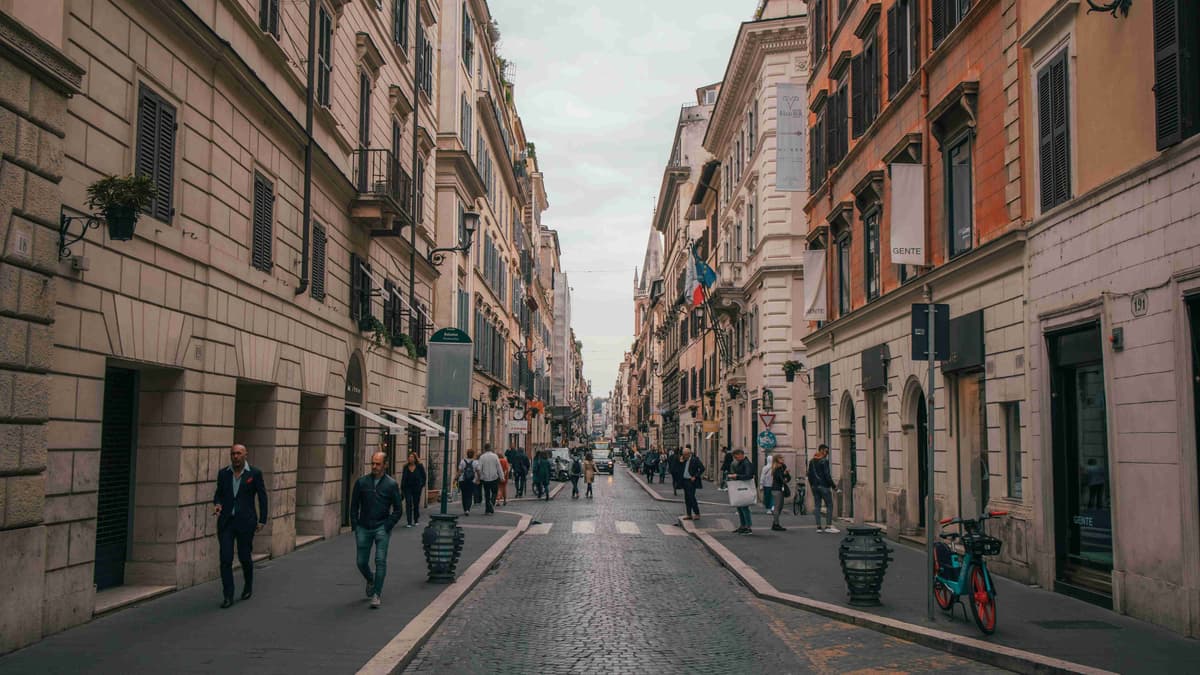 Chodci na dlážděné ulici lemované budovami v Římě.