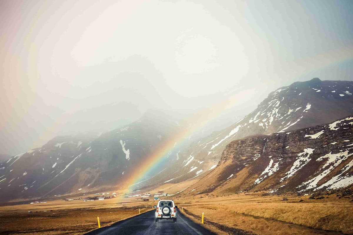 white-car-travelling-near-mountains-with-rainbow