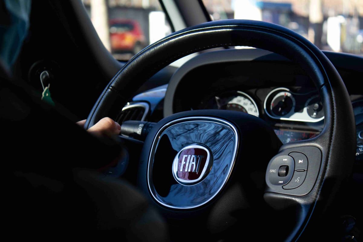 Driver's hand on a Fiat steering wheel with multimedia controls.