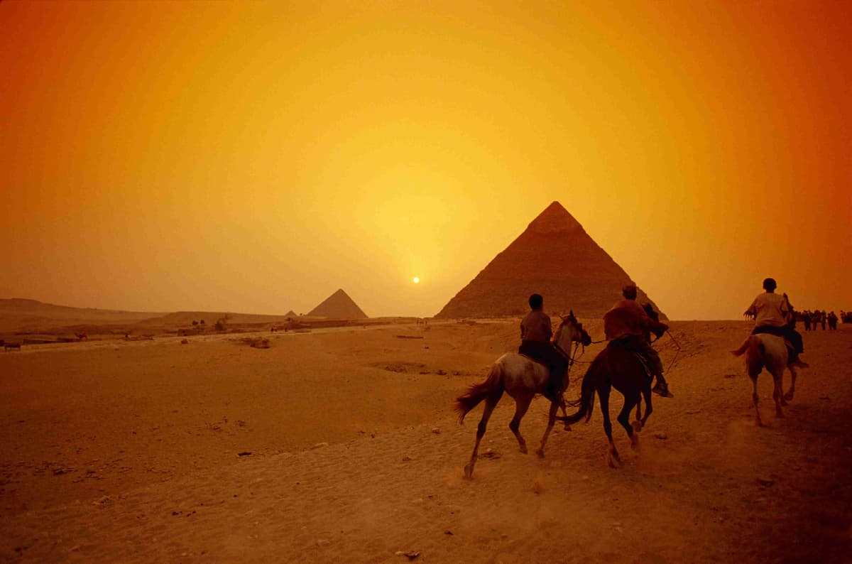 Cavalieri a cavallo vicino alle piramidi di Giza al tramonto