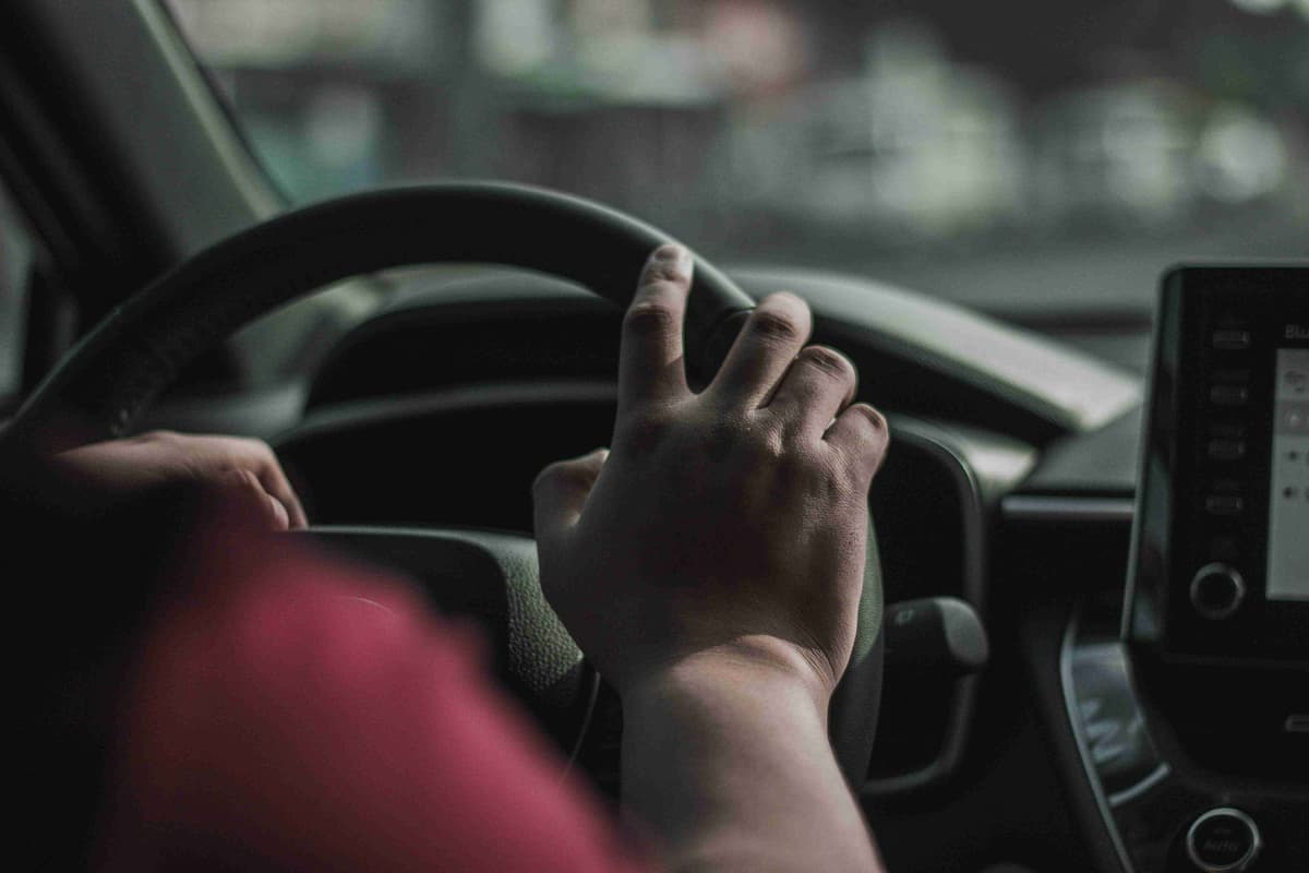 a person driving a car with their hand on the steering wheel