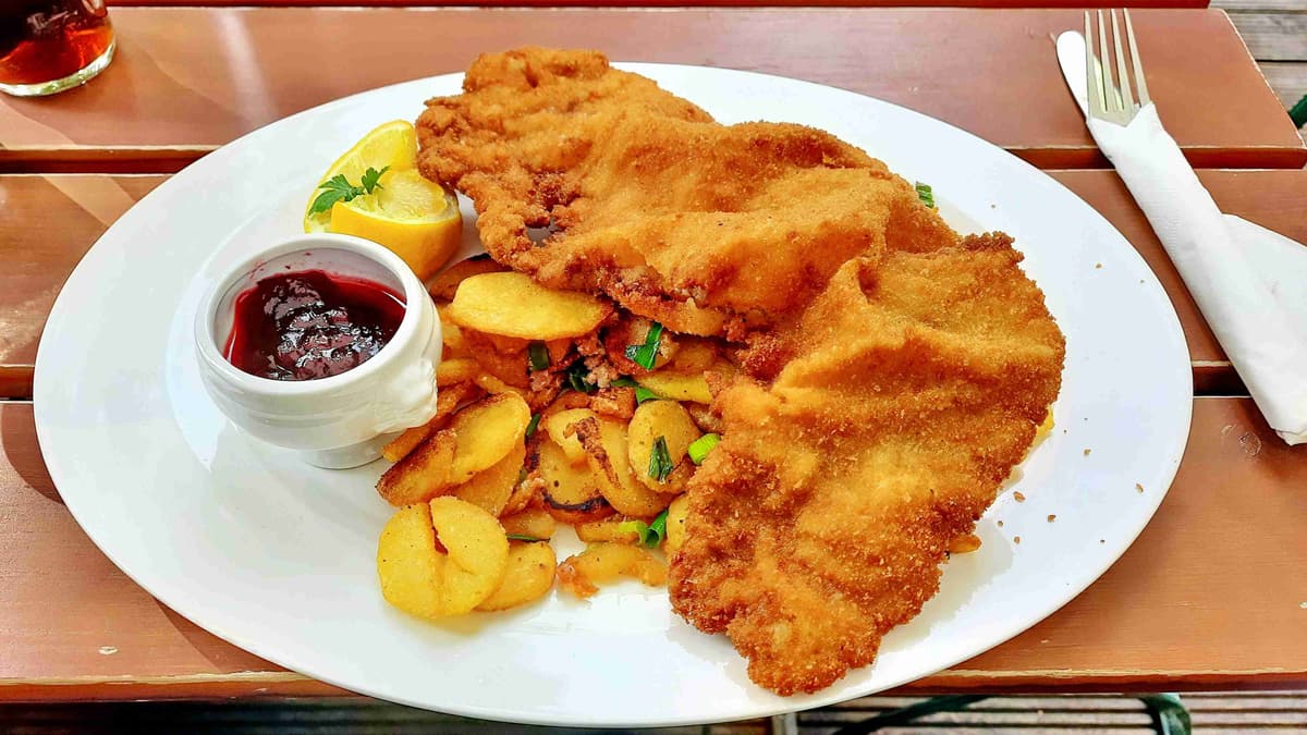 Tradicionālā šnicele ar ceptiem kartupeļiem un brūkleņu mērci