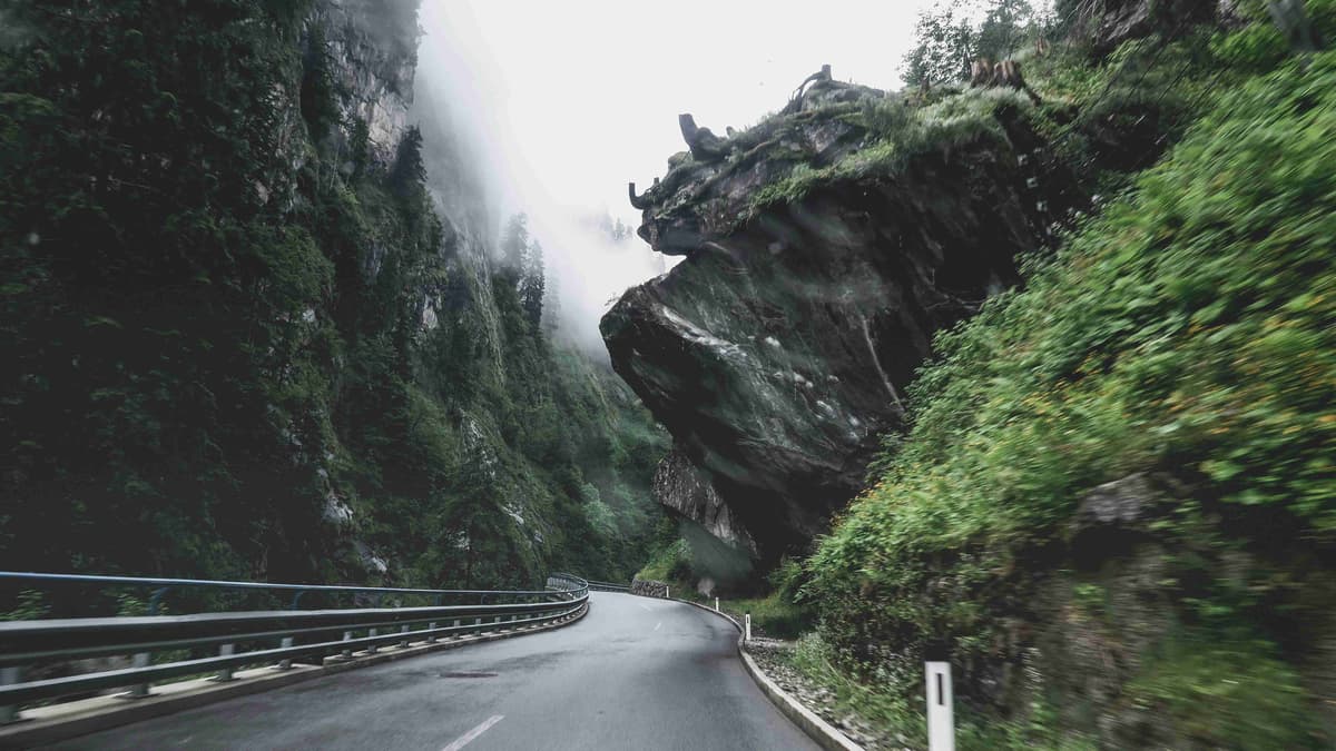 black-asphalt-road-between-green-and-brown-rocky-mountain-during-daytime