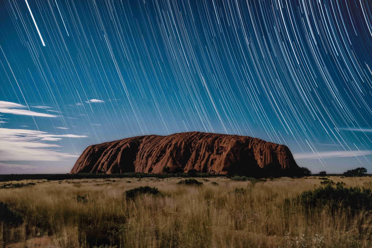 Uluru under star trails in the night sky.