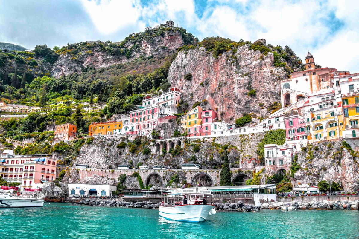 Boat on turquoise water with colorful Amalfi Coast cliffside buildings.